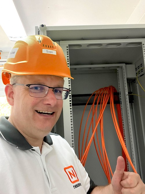 Nexave-Techniker Sven Albrecht vor einem Netzwerkschrank mit CAT7 Netzwerkkabeln